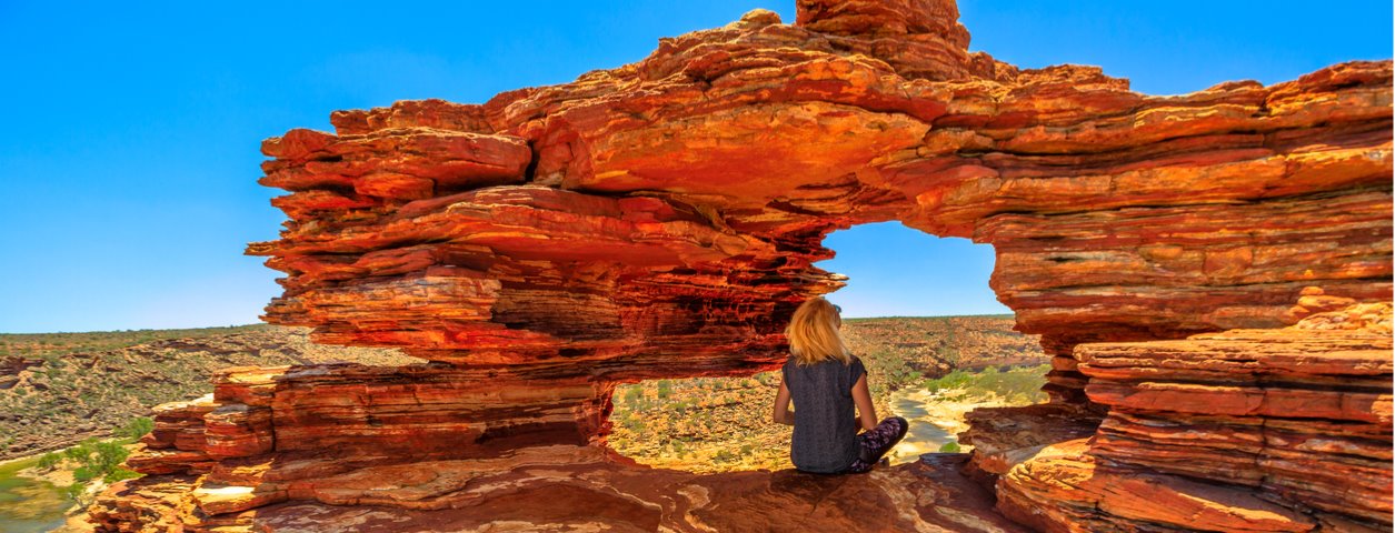 Woman sitting underneath the roof of a rock formation outdoors. 